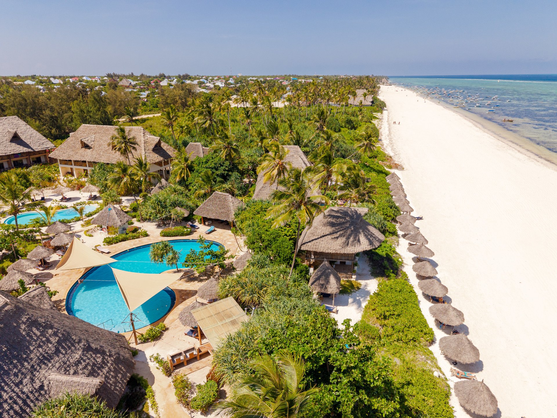 Wide aerial of the beach, thatched parasols, reef and open ocean
